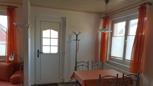 A room with a dining table, chairs, a sofa, a floor lamp, a coat rack, and a door with a window.