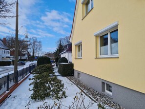 A residential building with a yellow facade, a paved pathway, and a snow-covered ground.