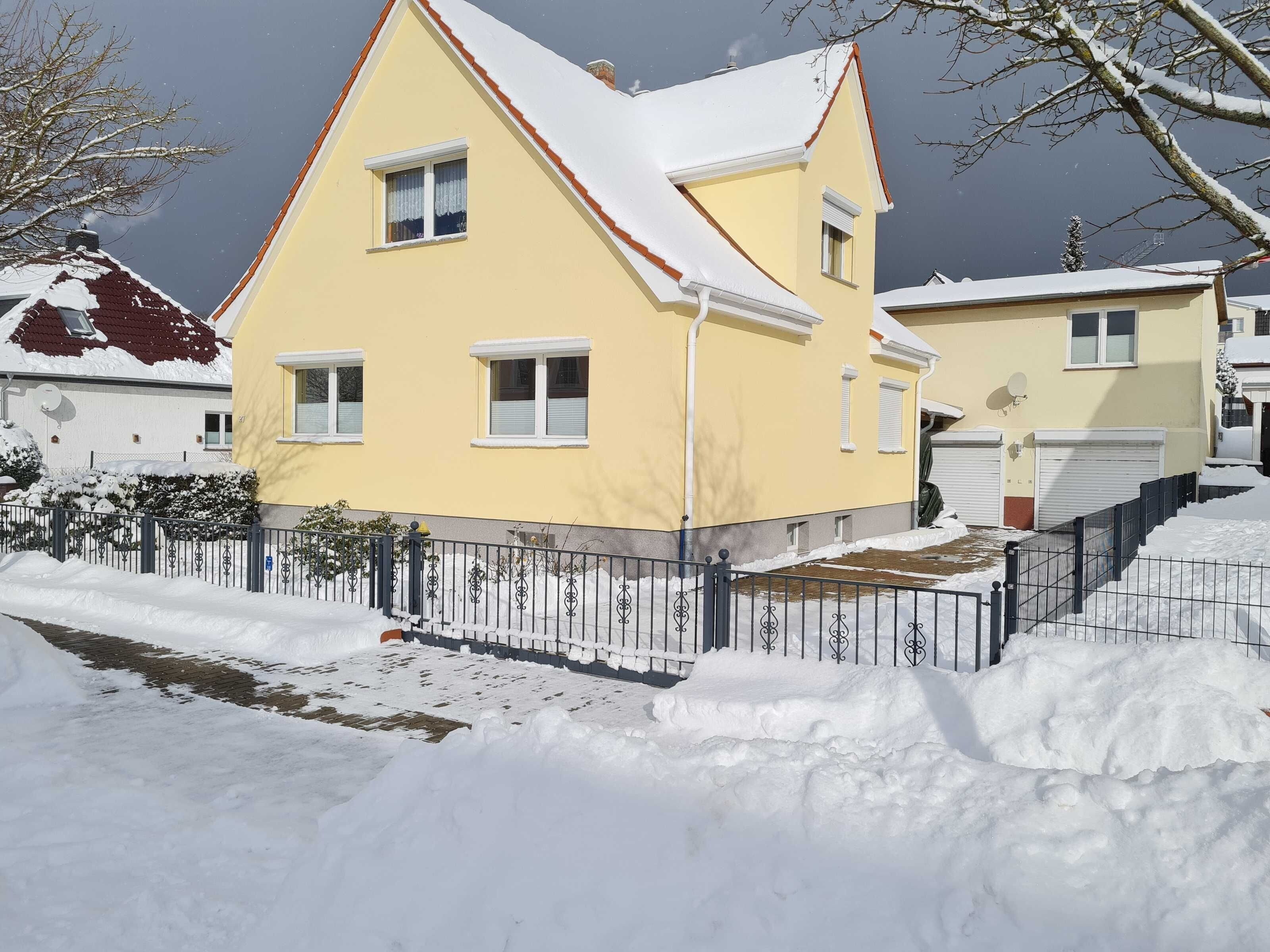 Ein gelbes, zweistöckiges Haus mit einem schneebedeckten Dach und einem schwarzen Metallzaun.