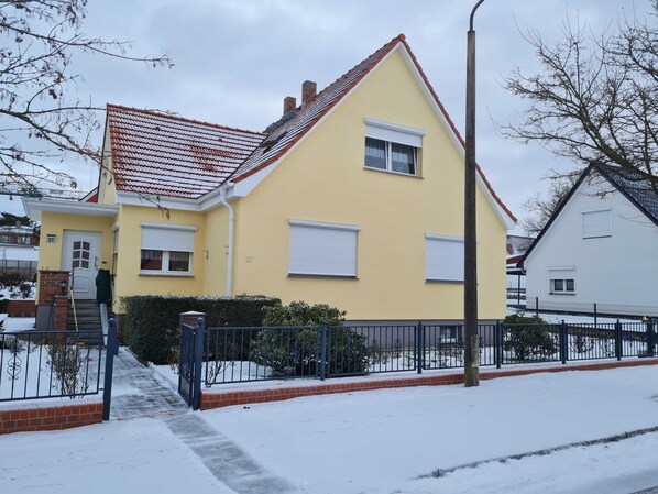 A yellow house with a red roof, white shutters, and a brick entrance.