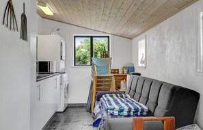 Cozy retreat with a kitchenette, sofa, and washing machine, offering a view of lush greenery.
