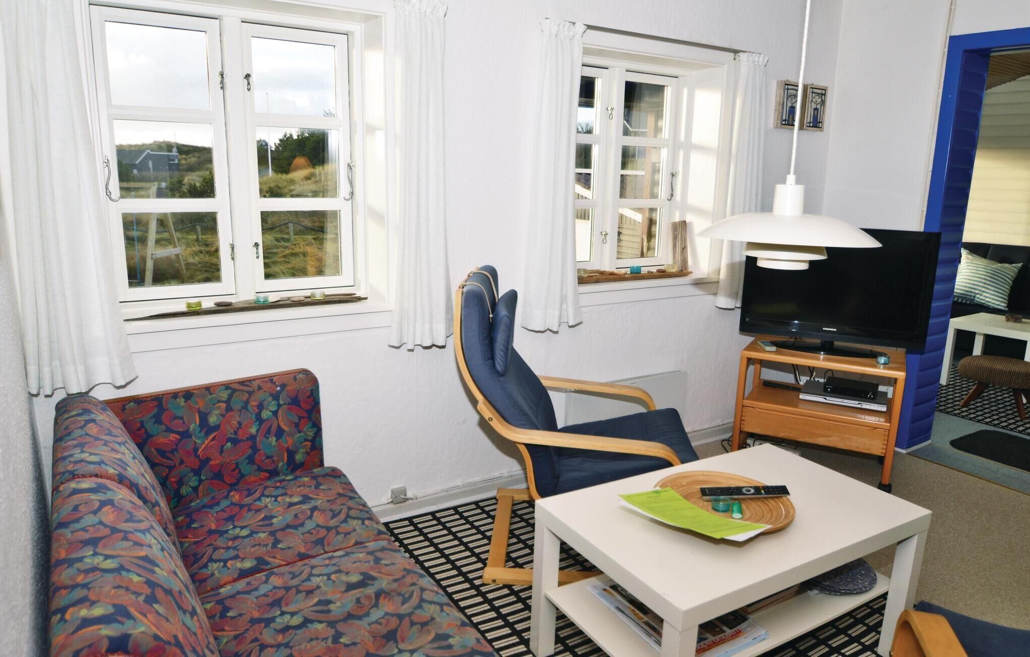 Una habitación pequeña y bien iluminada con un sofá, una silla, un televisor y una mesa con un control remoto.