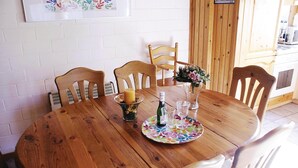 A wooden dining table with four chairs, a candle, a bottle, and a vase with flowers.