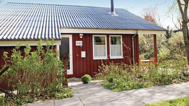 A small red wooden house with a metal roof, a chimney, and a number '145' on the door.