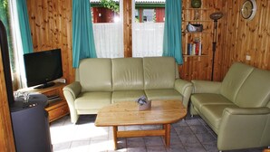 A cozy living room with a beige leather sofa, a wooden coffee table, and a television on a wooden stand.