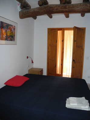 A bedroom with a bed, a red pillow, a wooden door, and a painting on the wall. - Romantically authentic, lots of space, great views, fiber optics for remote working (Torroja del Priorat)