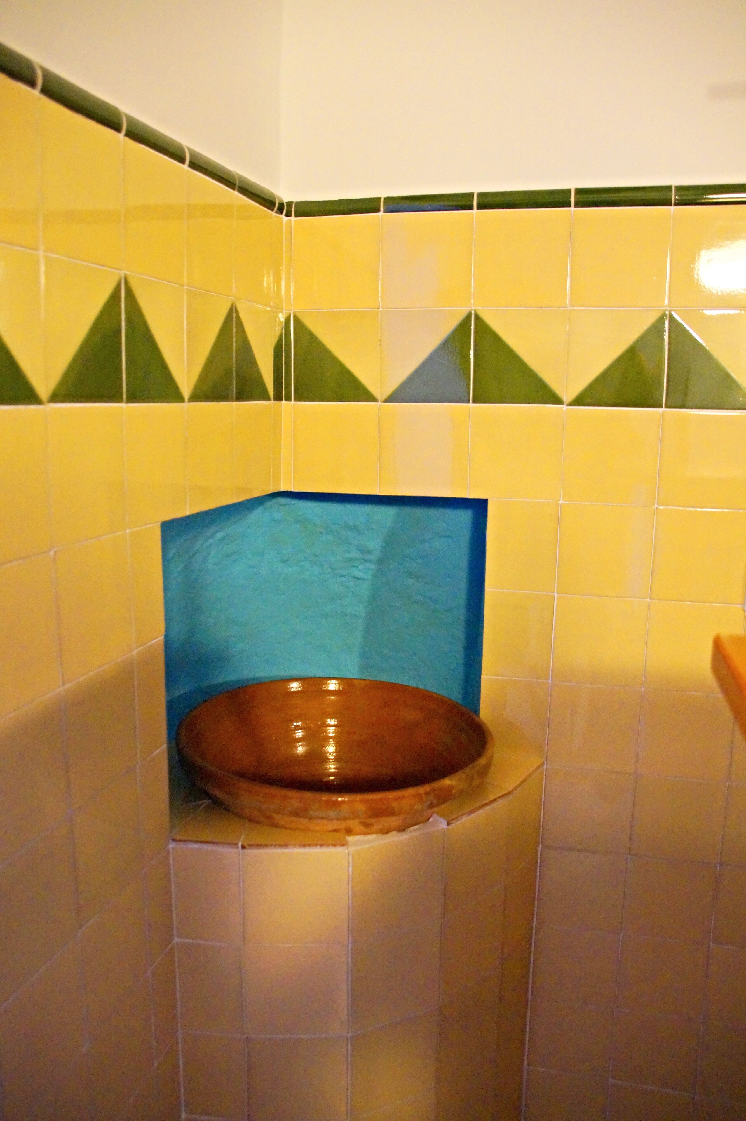 Une salle de bain avec des carreaux jaunes et verts, un lavabo marron et un coin recouvert de carreaux bleus.