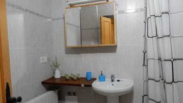 Een badkamer met een wit wastafel, een spiegel, een houten plank met toiletartikelen en een paarse prullenbak.