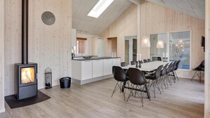 Une cuisine moderne dotée d’un îlot central, d’un coin repas avec une longue table et des chaises, et d’un poêle à bois.