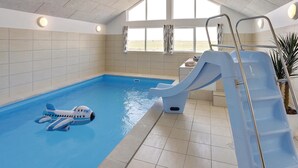 Une piscine intérieure avec un toboggan, un poste de surveillance pour le sauveteur et un petit bateau gonflable.
