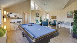 Une table de billard dans une pièce aux murs en bois, avec un coin bar et une table de baby-foot.