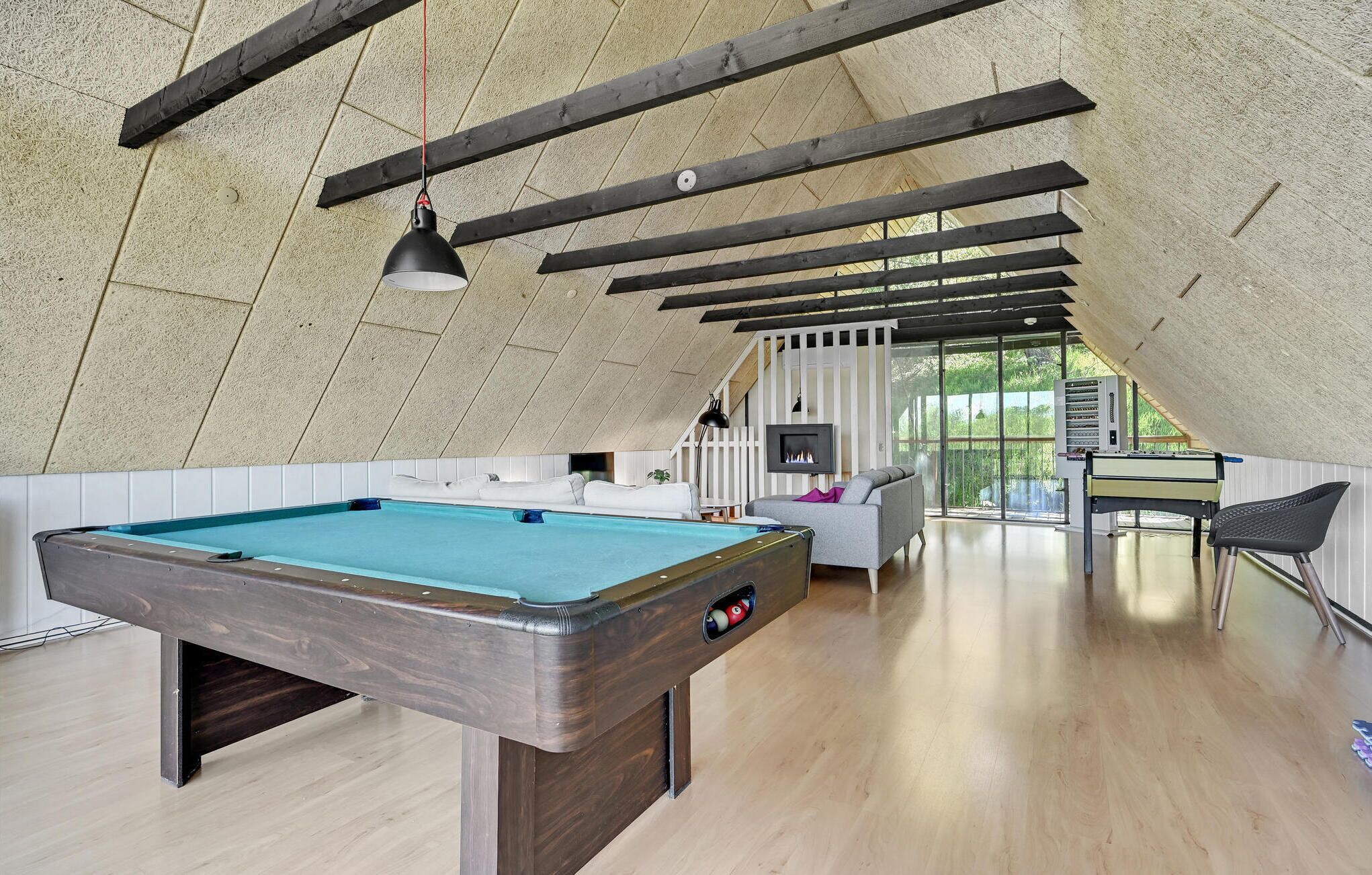Una mesa de billar en un espacio loft moderno y abierto, con vigas de madera y techo alto.