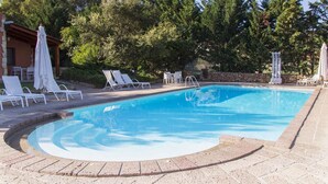 A swimming pool with a curved edge, surrounded by lounge chairs and umbrellas. - Studio with swimming pool and air conditioning (Alghero)