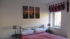A bedroom with a bed, two bedside tables, a window with curtains, and three wall-mounted paintings.