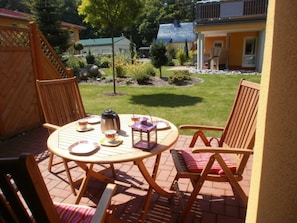 An outdoor patio with a round table and four chairs, a coffee pot, cups, and a lantern.