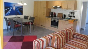 A compact kitchen with wooden cabinets, a dining area with a table and chairs, and a striped sofa.