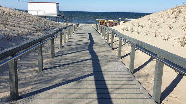 A wooden boardwalk leading to a beach with a white building and beach chairs.