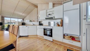 Eine moderne Küche mit weißen Schränken, einem eingebauten Backofen und einem Essbereich mit Holztisch und -stühlen.