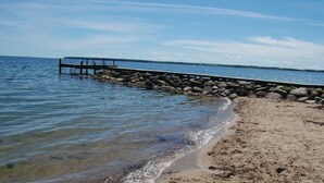 Ein Strand mit einem hölzernen Steg, der sich über ruhiges Wasser erstreckt, umgeben von einer felsigen Küstenlinie.