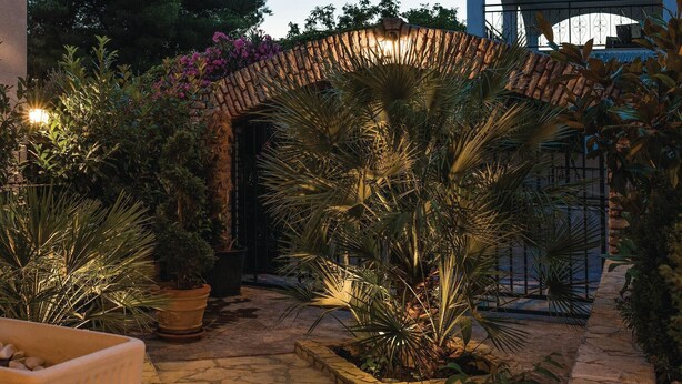 Ein Garten mit Kieswegen, Topfpflanzen und einem Zierbogen.