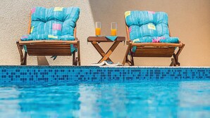 Zwei Liegestühle mit blauen Kissen und ein kleiner Tisch mit zwei Orangensäften am Pool.