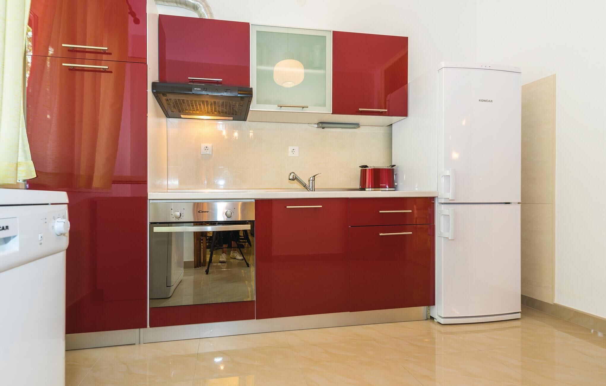 A compact kitchen with red cabinetry, a built-in oven, a refrigerator, and a small countertop.