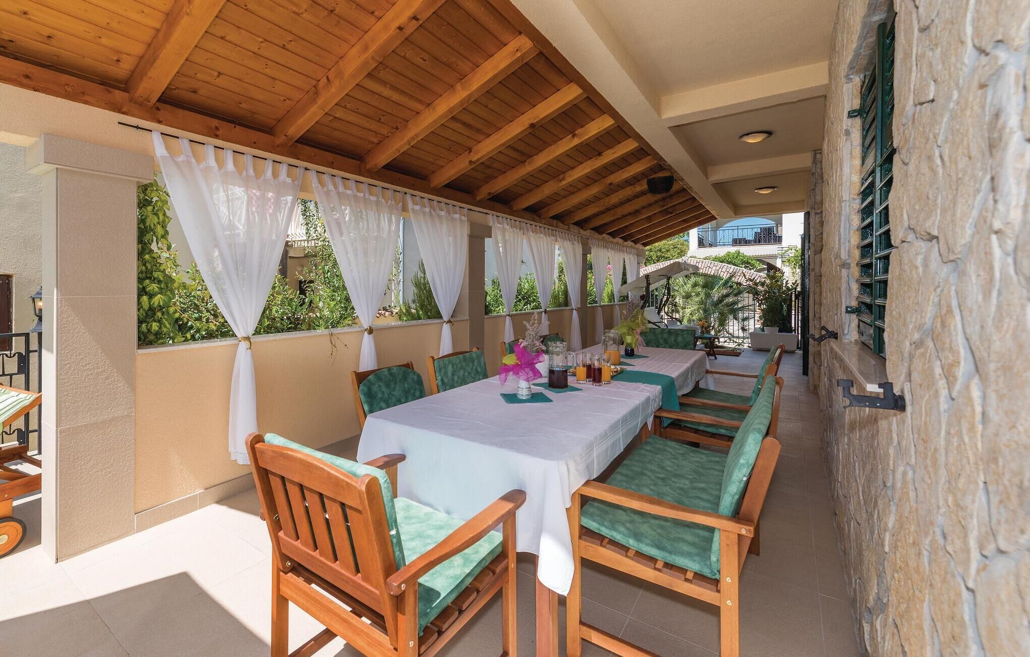 A covered outdoor dining area with wooden tables and chairs, white tablecloths, and a stone wall.