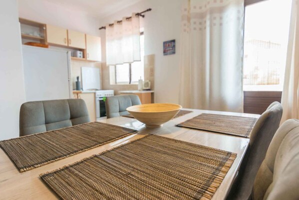 Un coin repas avec une table dressée pour quatre personnes, comprenant un grand saladier et des sets de table.