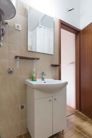 Un baño con lavamanos blanco, espejo y estante de madera arriba.