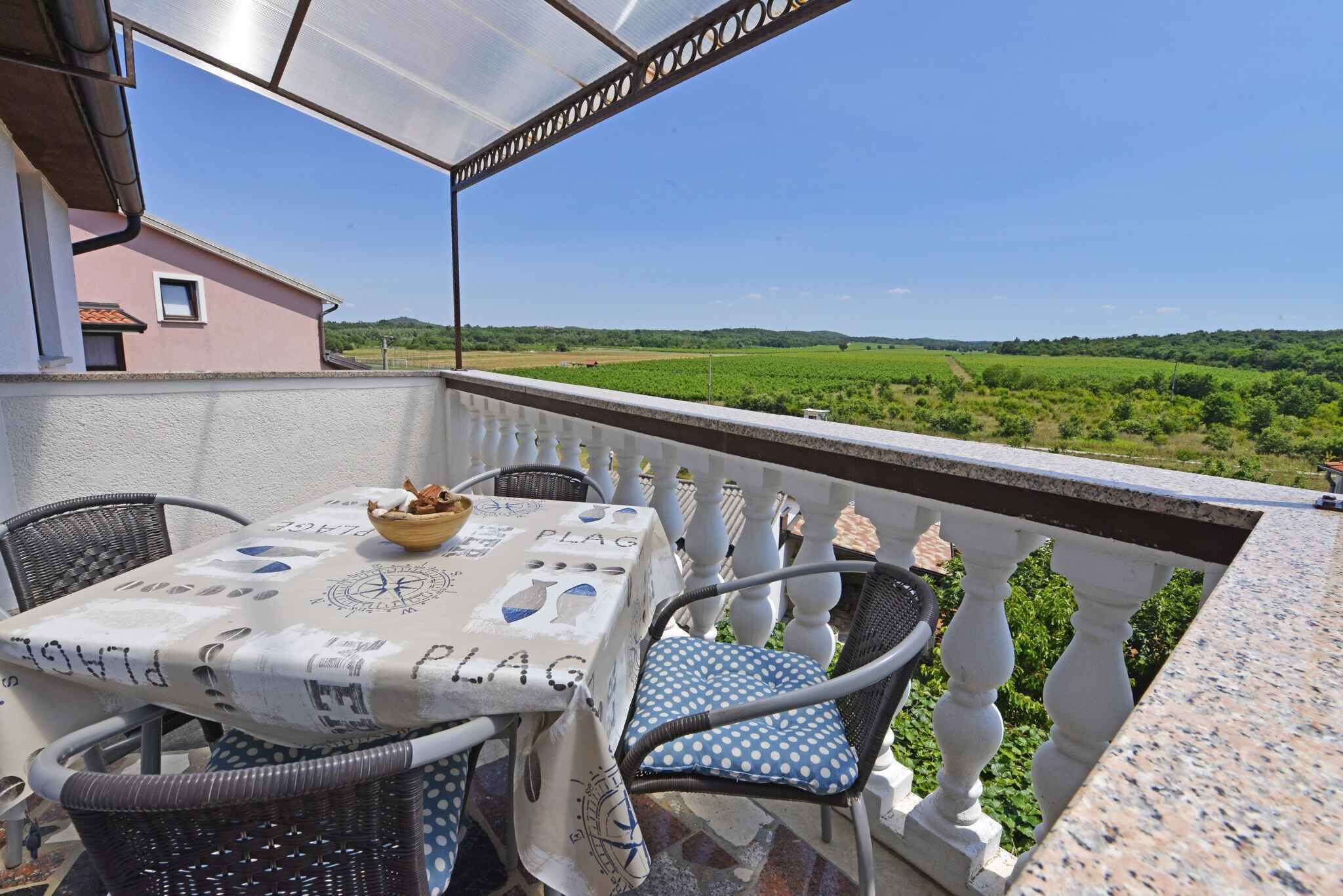 A balcony with a table and chairs, overlooking a green landscape.