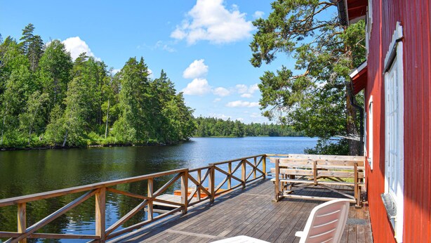 Una terraza de madera con barandilla que da a un lago, rodeada de árboles.