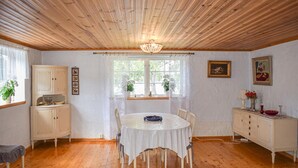 Comedor con una mesa redonda, cortinas blancas, techo de madera y una ventana con plantas.