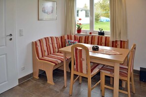 A dining area with a wooden table and striped upholstered chairs, a bench, and a window with curtains.