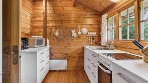Une cuisine compacte aux murs en bois, aux armoires blanches et dotée d’une fenêtre donnant sur un paysage verdoyant.