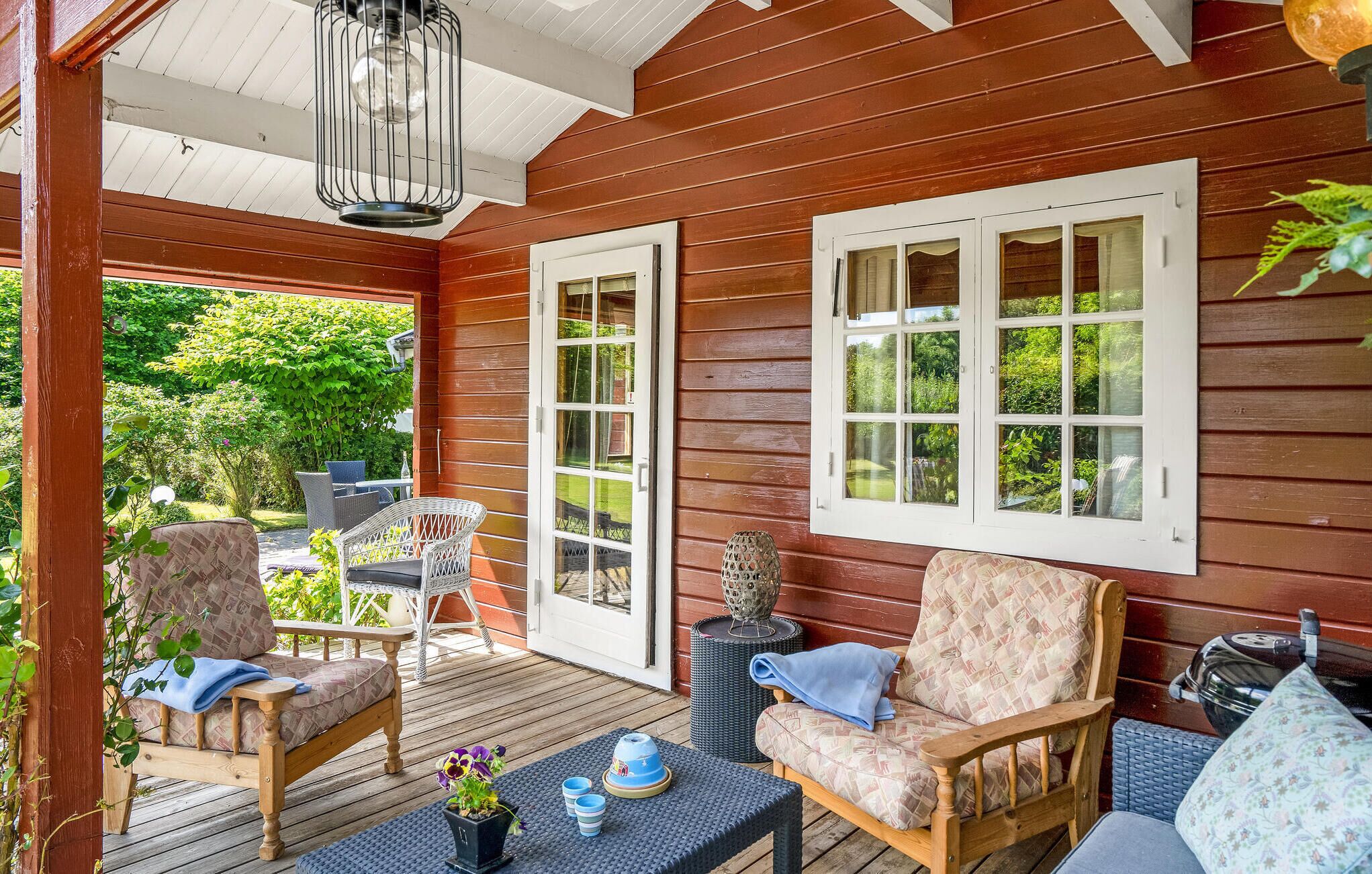 A wooden deck with outdoor furniture, including chairs and a table, and a view of greenery in the background.