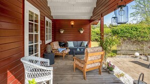 Une véranda en bois avec des fauteuils en osier, un canapé et des lanternes suspendues.