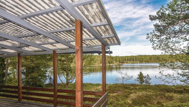 Eine überdachte Holzterrasse mit Blick auf einen ruhigen See und Wald.