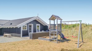Ein Strandhaus mit Spielbereich, inklusive Rutsche und Schaukeln.