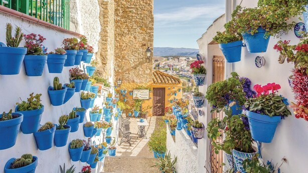A narrow street with blue potted plants on the walls, a stone building, and a view of the town. - Beautiful home in Iznájar (Iznájar)