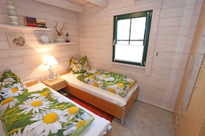 Une chambre confortable, aménagée dans le style d’un chalet, avec deux lits, une fenêtre et une étagère où sont posés des livres et des objets décoratifs.
