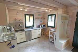 Une cuisine équipée d’un évier, d’une cuisinière, d’un four à micro-ondes et de placards. Il y a deux fenêtres avec des cadres verts et une porte dotée d’une poignée.