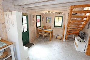 Une cuisine compacte avec un coin repas, un escalier en bois et une petite télévision posée sur un meuble blanc.