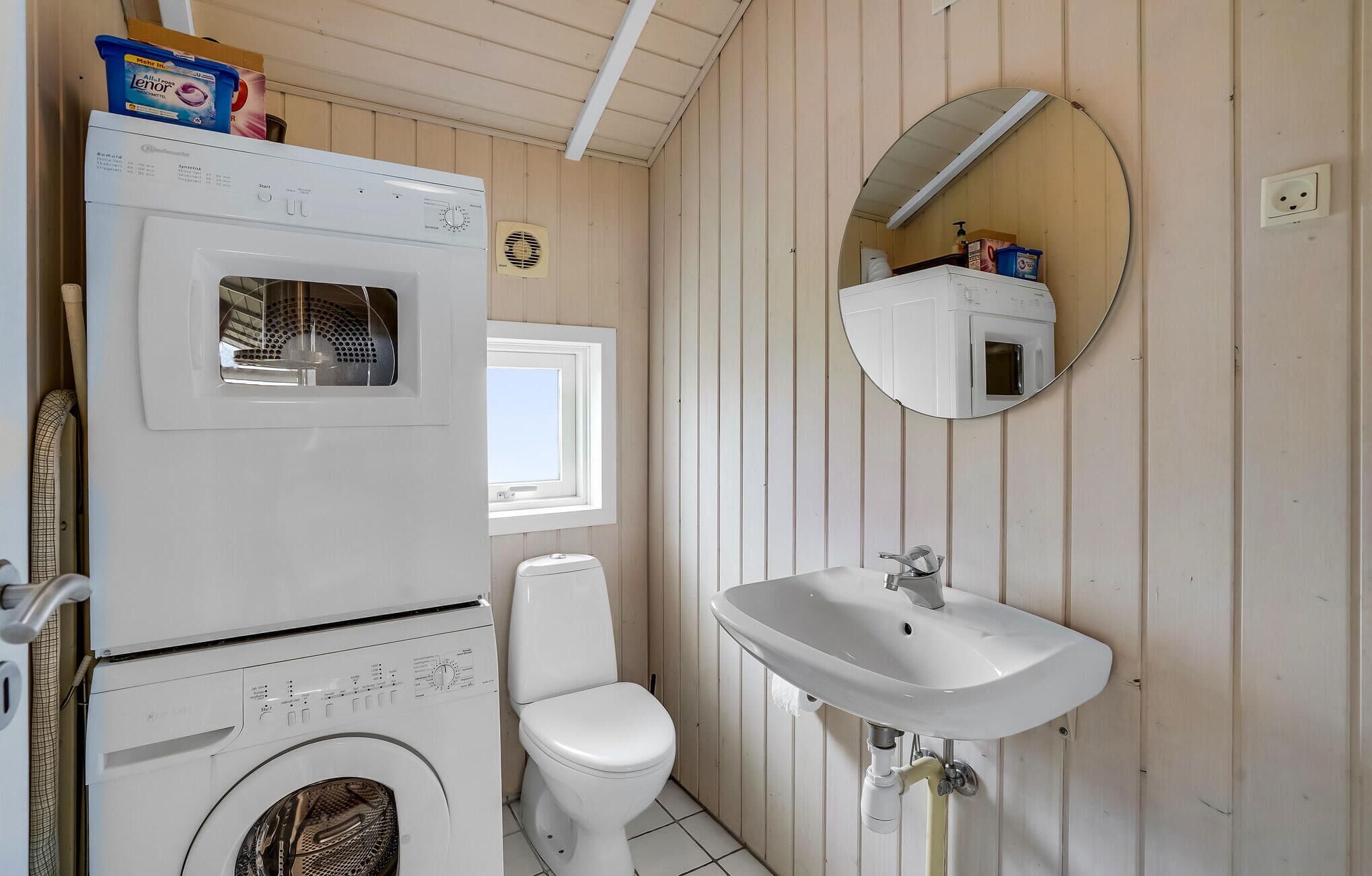 Une petite salle de bain équipée d’un lave-linge, de toilettes, d’un lavabo et d’un miroir.