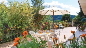 Patio esterno con tavolo apparecchiato per mangiare, immerso nel verde e decorato con una statua.