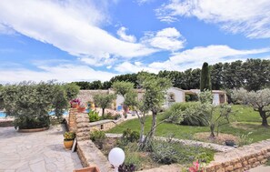 A garden with a stone pathway, potted plants, and a small building with a pool in the background.