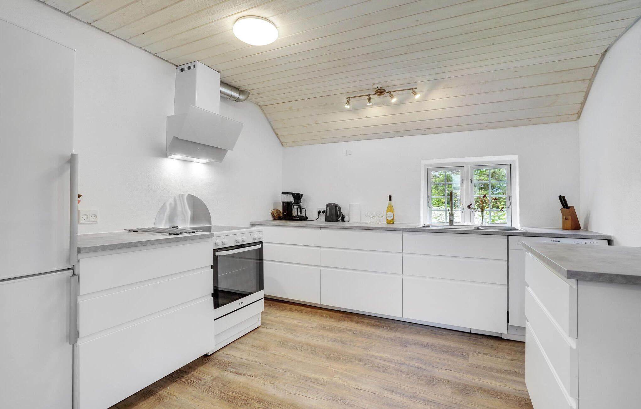 A modern kitchen with white cabinetry, a built-in oven, a stove, and a window with a view of greenery.