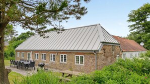 A stone building with a sloped metal roof, outdoor seating, and a garden area. - Stunning home in Ulfborg with sauna (Ulfborg)