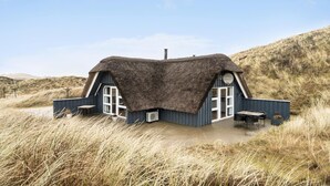 Ein Haus mit einem Reetdach, zwei großen Fenstern und einem kleinen Tisch davor.