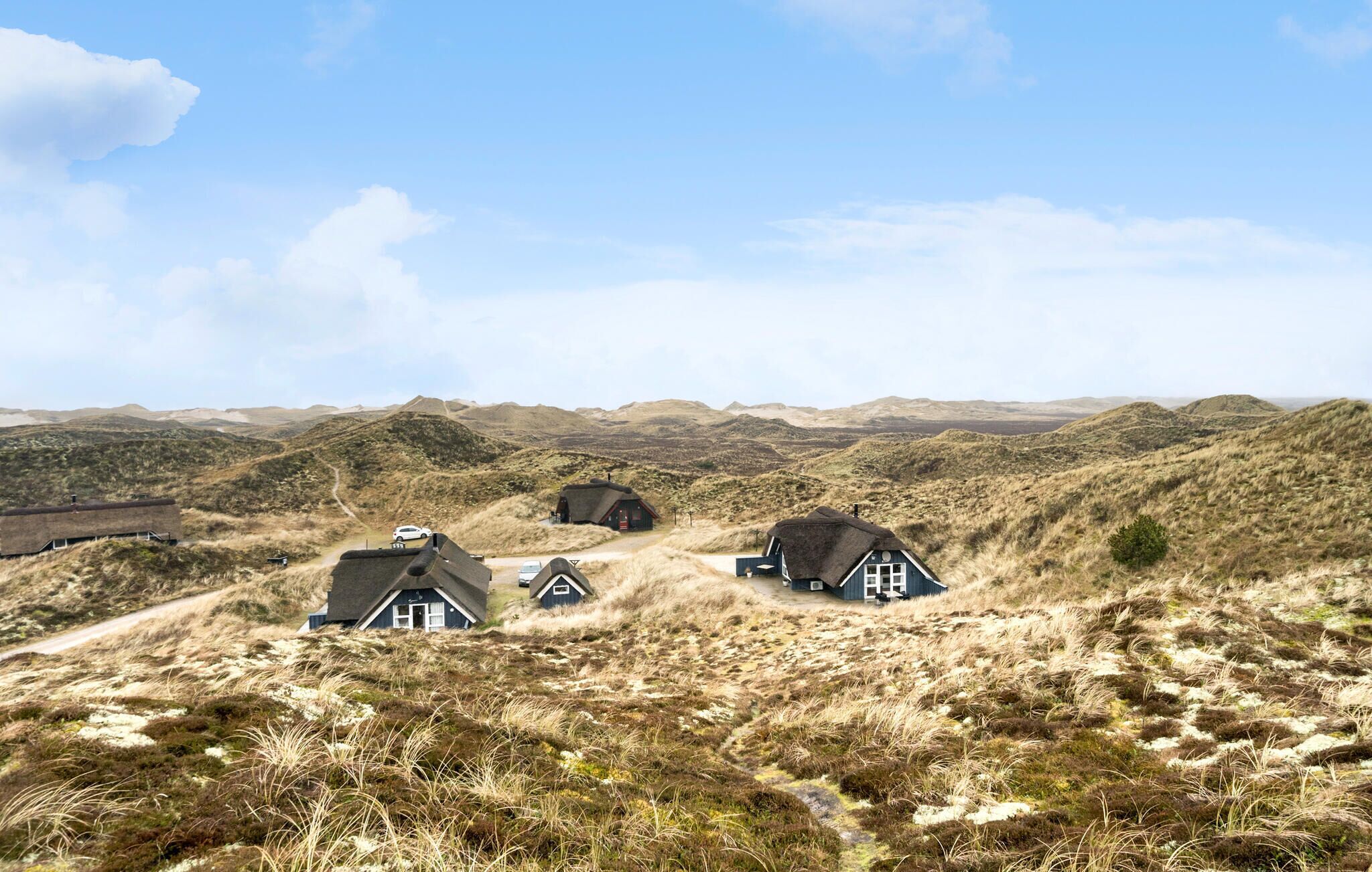A remote, thatched-roof house in a hilly, grassy landscape with a clear sky.