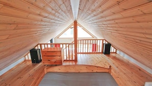 A high-ceilinged attic bedroom with wooden walls and a sloped roof, featuring a bed, a small staircase, and two speakers. - Amazing home in Annerstad with sauna (Annerstad)